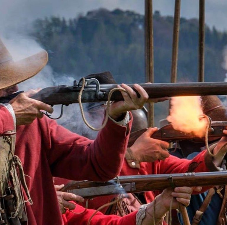 English Civil War reenactor firing a matchlock musket in a volley with other musketeers.
